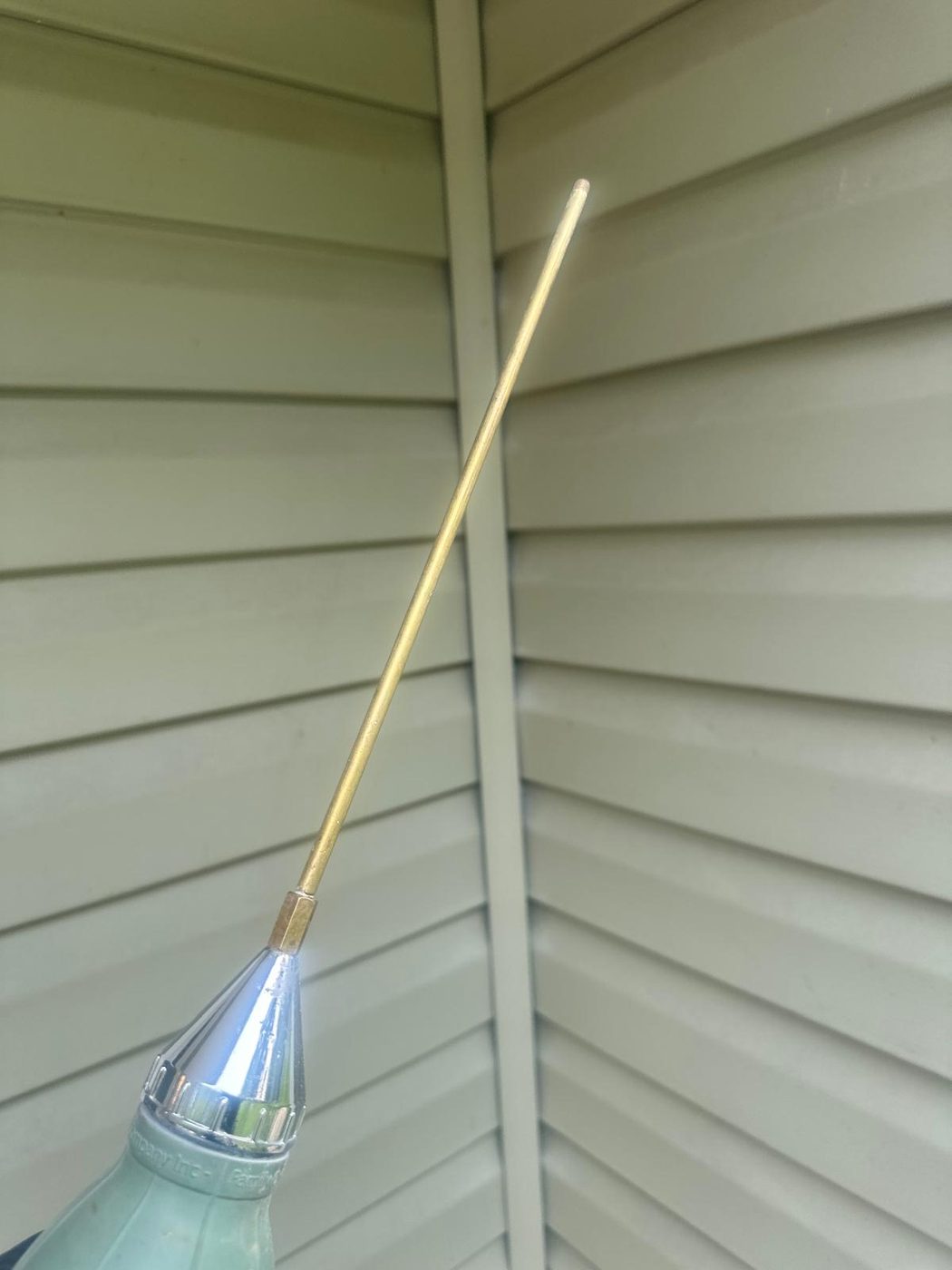 Close-up of a pest control sprayer wand and nozzle against a home's siding