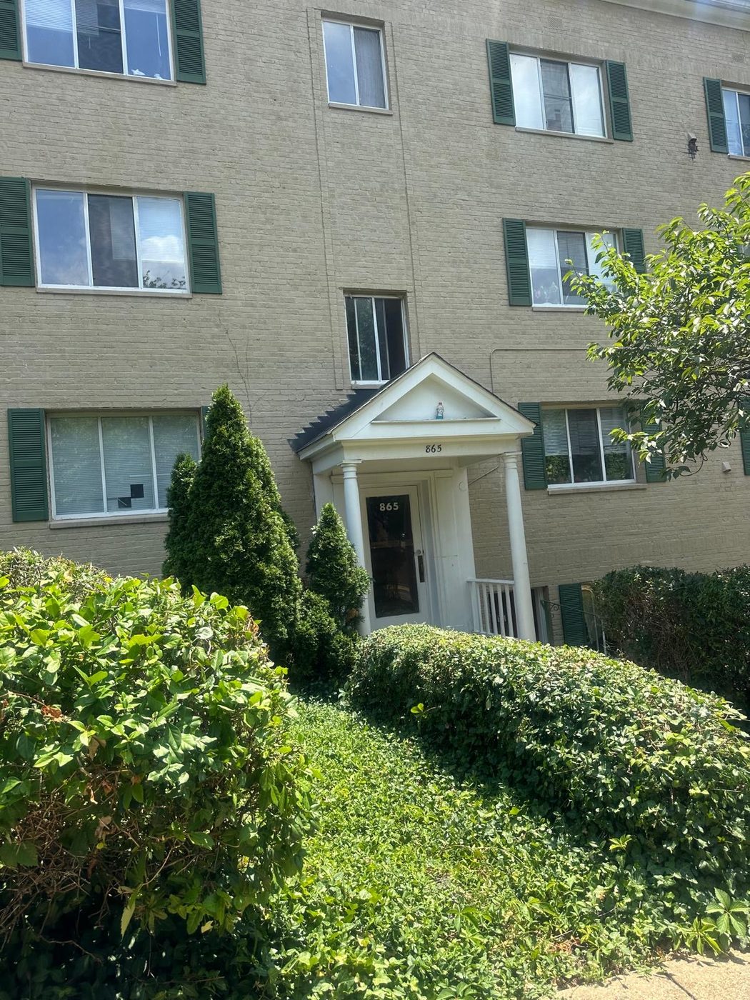 Entrance of a multi-family brick residential building with landscaping and shrubs