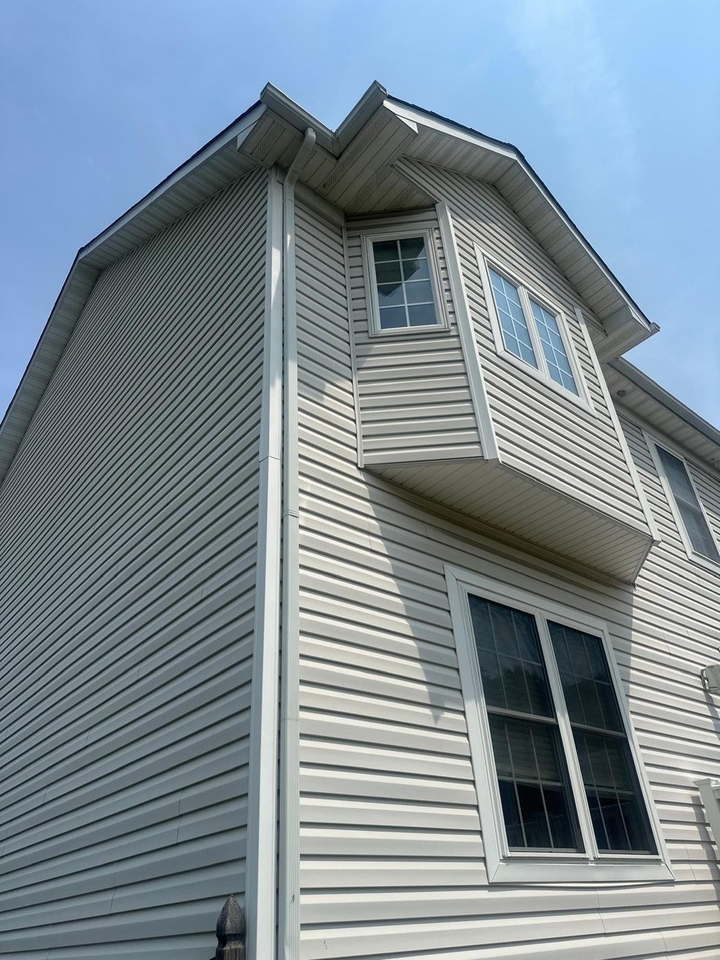 View looking up at a home's roofline, eaves, and vinyl siding against a blue sky