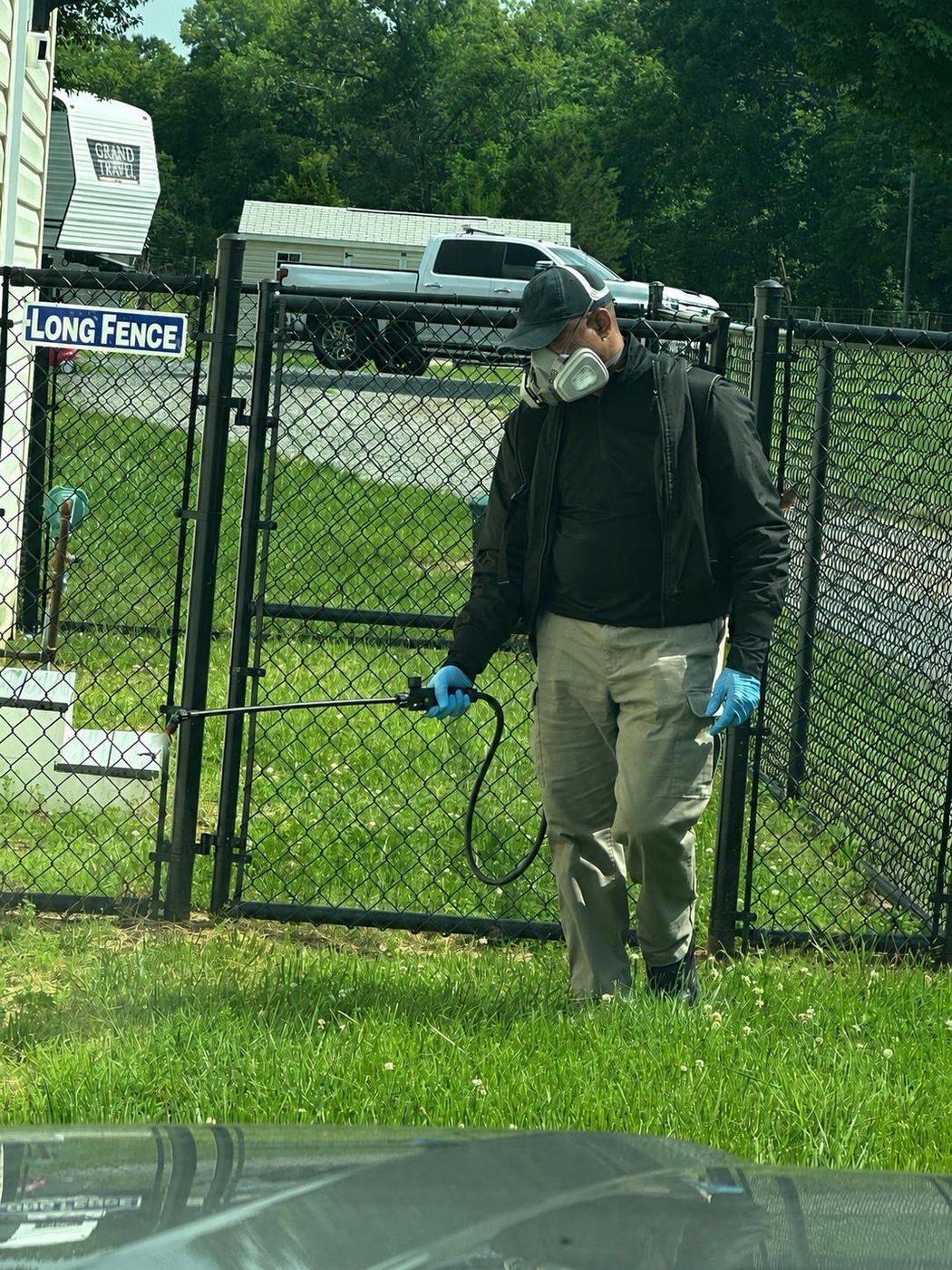 YourTurn Pest Solutions technician in respirator and gloves applying an exterior treatment along a yard fence line
